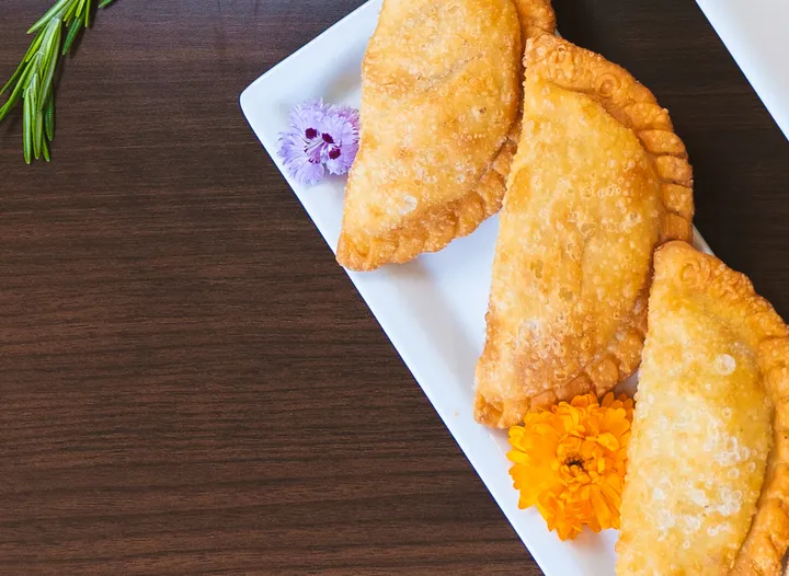 Golden empanadas with fresh peppers and herbs on a warm wood table