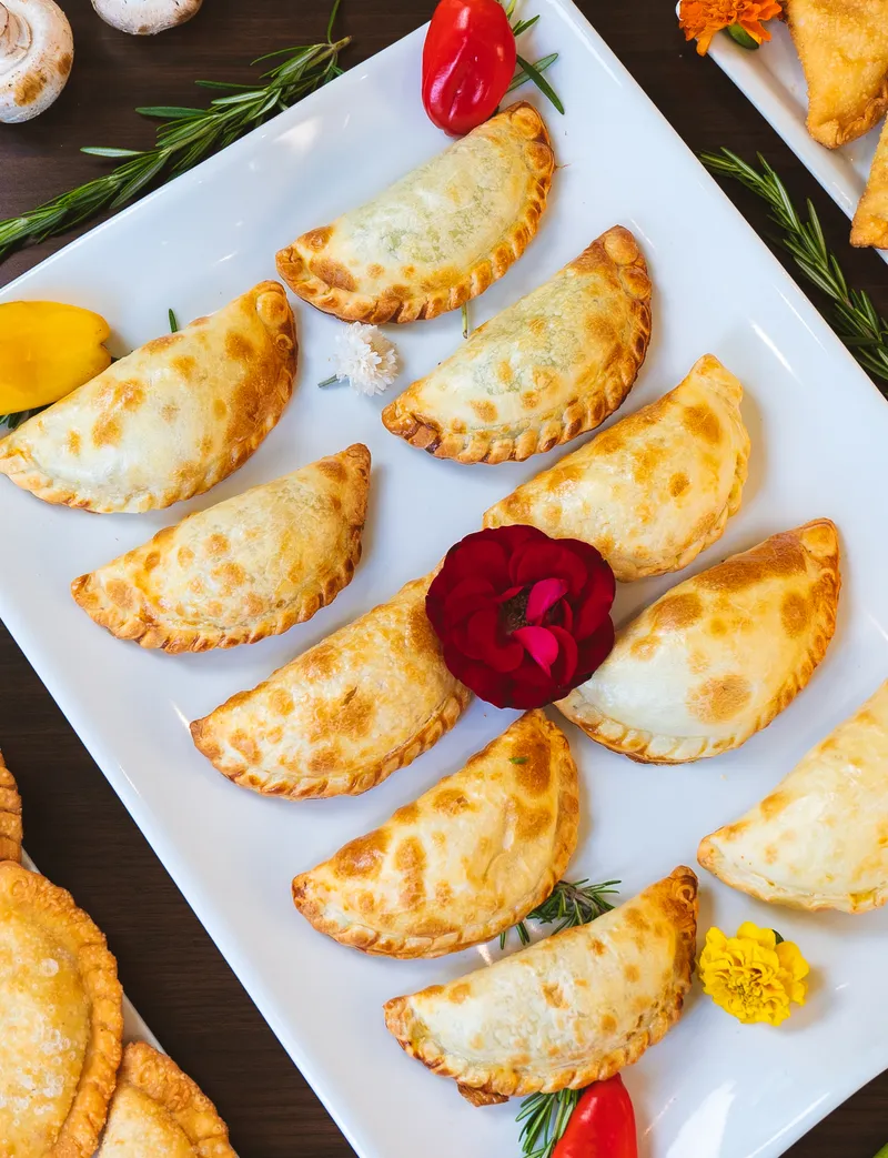 Rows of golden hand-crimped empanadas arranged on a white platter